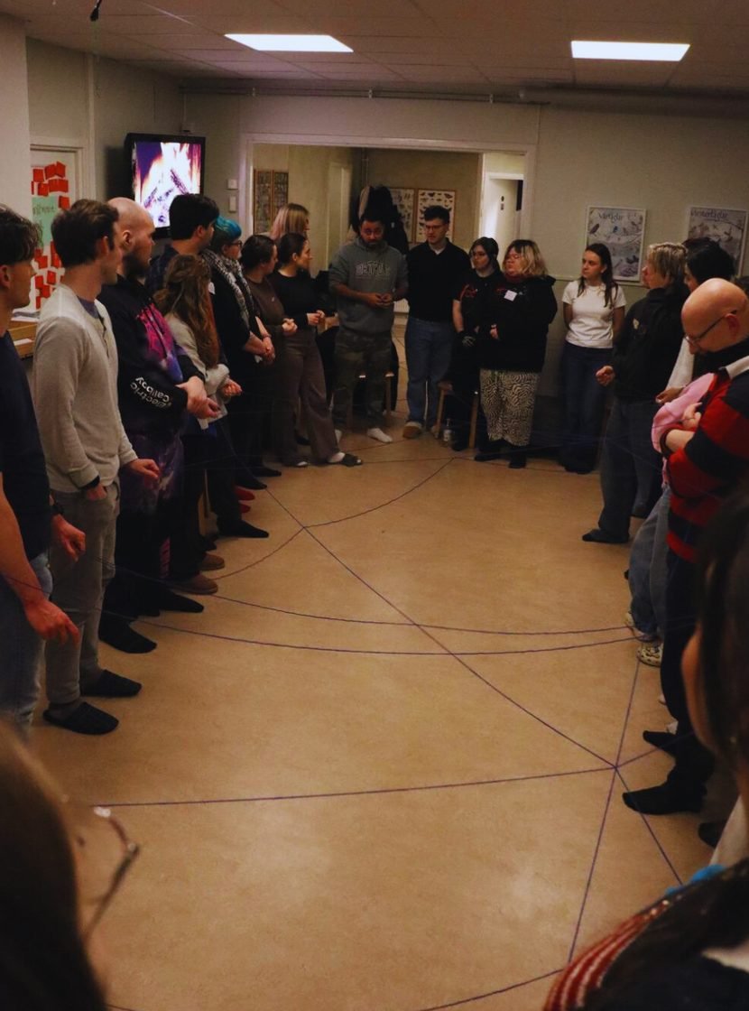 Participants standing in a circle around a web of string during a non-formal education session